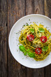Noodles with basil pesto, parmesan cheese, tomatoes and basil leaves served on wooden table 