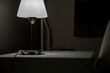 A bedside table and a burning lamp stands on it in a dark room. Hotel number.