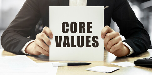 Poster - businessman holding a white card with text core values on office background