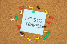 Let's Go Travel Text On Light Blue Post-it Paper Pinned On Bulletin Cork Board Surrounding By Multi Color Pins. This Message Can Be Used In Business Concept About Travel.
