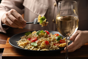 Woman eating delicious pasta with tomatoes and basil at wooden table, closeup