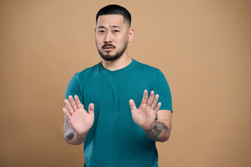 Wall Mural - Serious asian man with beard making stop gesture showing palms of hands
