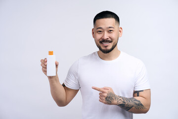 Wall Mural - Happy asian handsome man wearing white t shirt holding shampoo bottle isolated on white background