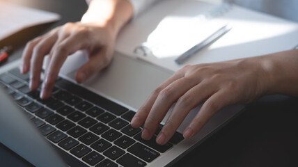 Wall Mural - closeup of woman hand typing, searching the information on laptop computer with a pen and notebook o