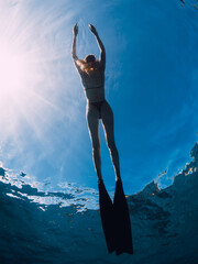 Wall Mural - Woman freediver relax with fins on the ocean surface. Freediving and sunlight in blue ocean