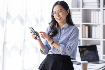 Wall Mural - Business Asian woman hold phone and use laptop at the workplace. Project stats financial data sales charts on laptop and cellphone Asian finance concept
