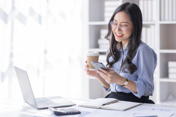 Wall Mural - Business Asian woman hold phone and use laptop at the workplace. Project stats financial data sales charts on laptop and cellphone Asian finance concept
