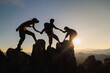 © Tinnakorn - silhouette of Teamwork of three  hiker helping each other on top of mountain climbing team. Teamwork friendship hiking help each other trust assistance silhouette in mountains, sunrise.