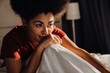 © Drobot Dean - Afro woman smiling and looking aside while while sitting on bed