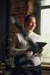© master1305 - Portrait of young, smiling, beautiful business woman standing near window, looking outside, working on tablet in her office. Concept of business, fashion, career development, profession, occupation