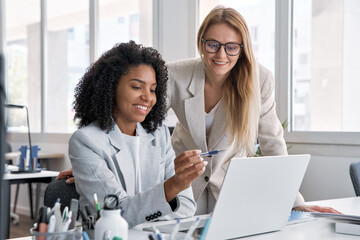 Wall Mural - Two businesswoman working together using digital laptop pc and talking about a business project. Small creative diversity team of African American and blond females executives meeting work in office.