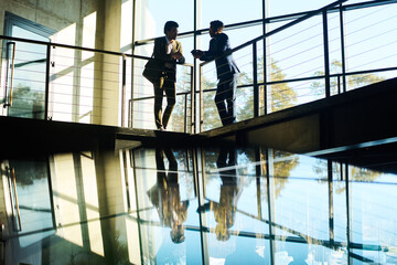 Wall Mural - Outlines of two young male colleagues in formalwear standing by railing against large window in office center and discussing working points