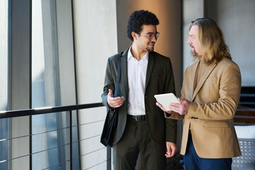 Wall Mural - Young smiling businessman explaining something to mature colleague with tablet during presentation or discussion of working points