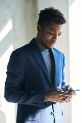 Poster - Young serious African American businessman in formalwear using mobile phone while texting in front of camera in sunlit corridor of office center