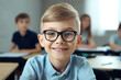 A small school boy wearing glasses sitting at the desk in classroom on the lesson, looking at camera. Generative AI