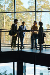 Poster - Working meeting of four intercultural employees in formalwear standing against large window in corridor of office center and brainstorming