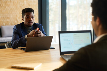 Poster - Confident African American male employer or HR manager with laptop talking to young applicant sitting in front of him during interview