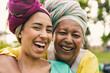 Happy african mother hugging adult daughter wearing traditional dress while smiling on camera