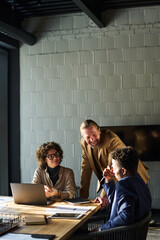 Poster - Three intercultural brokers gathered for meeting by desk having discussion of working points or strategies or preparing report for conference