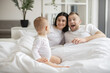 © Sofiia Shunkina - Focus on adorable little child sitting on white soft duvet and watching her parents playing roles of book characters on Sunday morning at home. Concept of family and togetherness.
