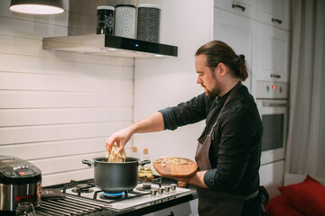 A male cook is cooking at the stove at home in the kitchen