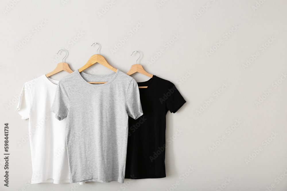 Stylish t-shirts hanging on grey wall