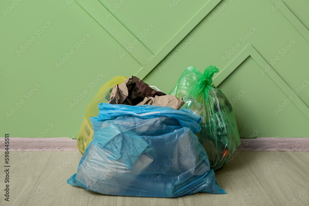 Full garbage bags near green wall