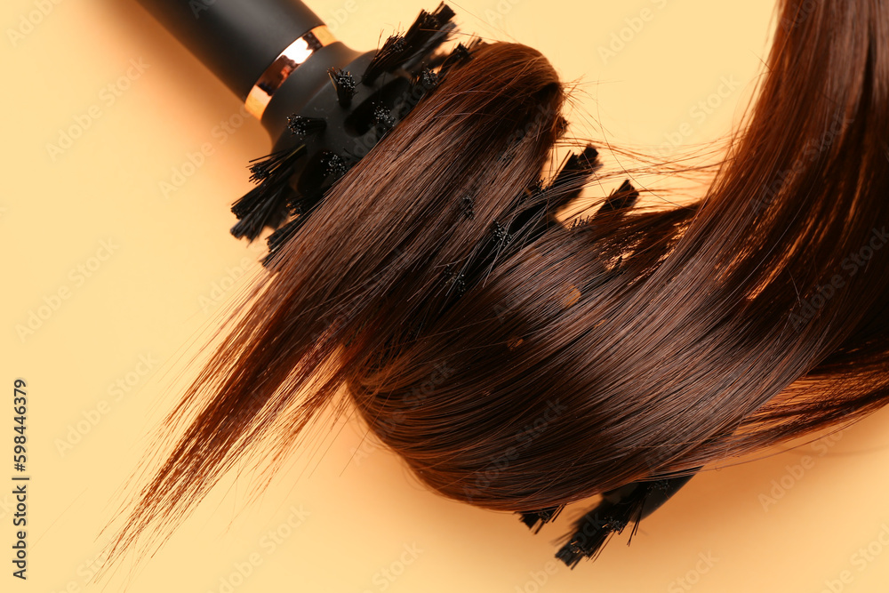 Brown hair with round brush on yellow background, closeup