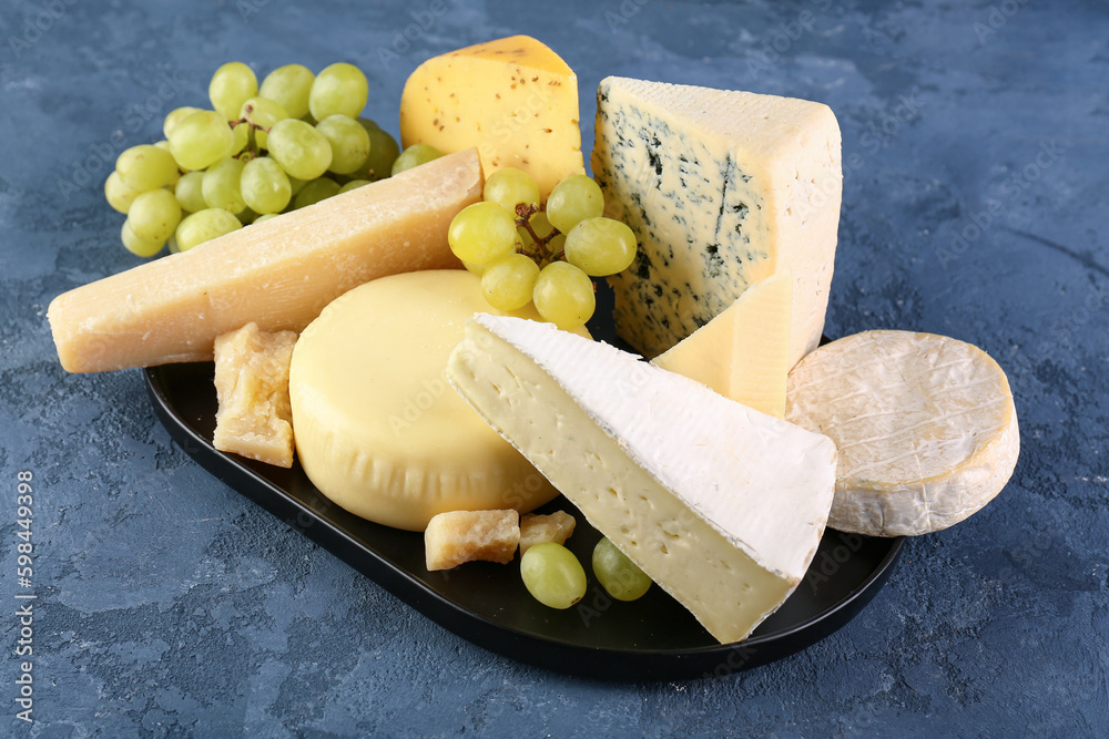Plate with different types of cheese on blue background