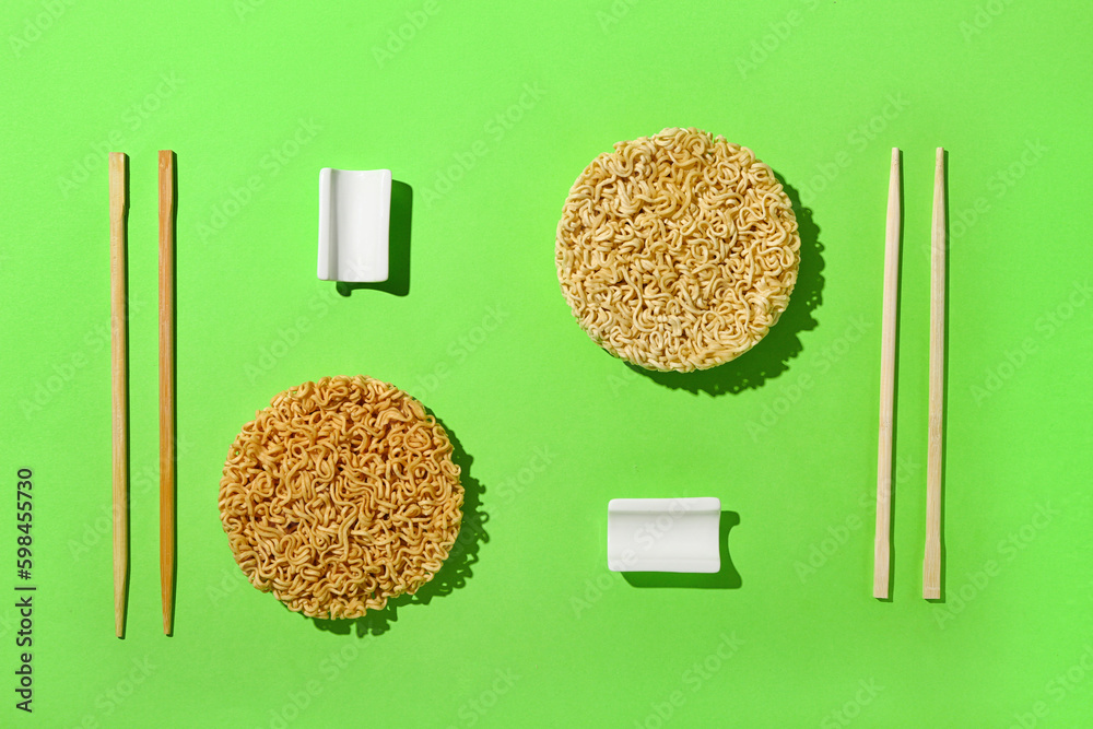 Raw instant noodles with wooden chopsticks on light green background
