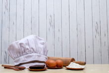 Chef Hat With Cooking Ingredients On Kitchen Wooden Table