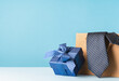 Happy Fathers Day background banner. blue gift box and brown paper bag, necktie, glasses on pastel blue table.