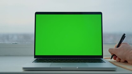 Aufkleber - man writing in notebook near laptop with green screen workplace with big window at home or office Generative AI
