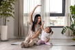 Young fit long hair mother exercise with her two year old child at home near the window