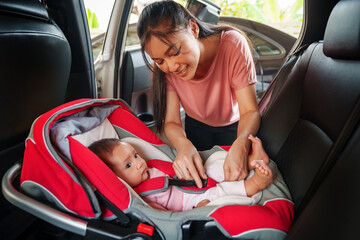 happy mother is fastening safety belt to newborn baby in car seat