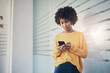 © Flamingo Images - Young businesswoman texting on her phone while leaning against a glass wall