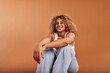 © Flamingo Images - Smiling woman wearing a tank top and jeans sitting on an orange backdrop
