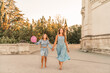© svetograph - Daughter mother run holding hands. In blue dresses with flowing long hair against the backdrop of a sunset and a white building.