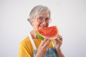 Wall Mural - Smiling attractive old senior woman holding a slice of fresh watermelon looking at camera isolated on white background - healthy eating lifestyle concept