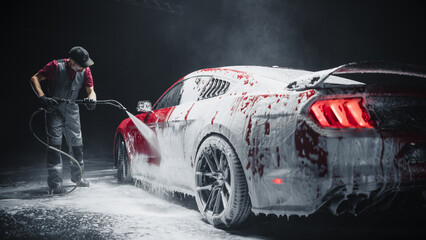 Automotive Detailer Washing Away Smart Soap and Foam with a Water High Pressure Washer. Red Performance Car Getting Care and Treatment at a Professional Vehicle Detailing Shop