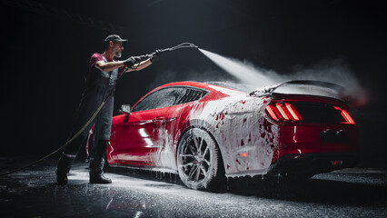 Automotive Detailer Washing Away Smart Soap and Foam with a Water High Pressure Washer. Red Performance Car Getting Care and Treatment at a Professional Vehicle Detailing Shop
