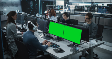 Fototapete - Group of Diverse Multicultural Men and Women Working on Desktop Computers in a Research Center. Young Software Developer Working on a Computer with Two Green Screen Mock Up Displays