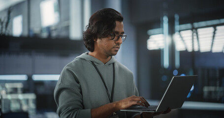 Portrait of a Technological Software Engineering Department Manager Standing and Using a Laptop Computer. Indian Female Focused on Thinking while Working in the Office