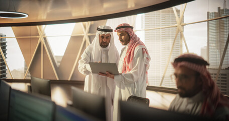 Wall Mural - Two Young Muslim Financial Advisers Use Laptop Computer to Discuss a Stock Market Strategy in a Modern Industrial Office. Arab Managers Work in a Banking Research and Development Center