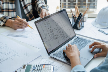 Engineers looking and discussing over blueprints on desk.