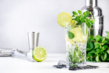 Wall Mural - Mojito summer alcoholic cocktail drink with lime, white rum, soda, cane sugar, mint, and ice in highball glass on gray background.  Steel bar tools. Copy space