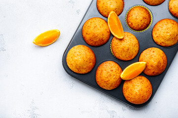 Sweet orange muffins in baking dish on white table background, homemade pastries, top view, copy space