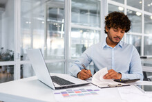 Serious And Concentrated Financier Businessman Inside Office At Workplace Sitting At Table And Signing Contract Account Documents, Successful Hispanic Man In Shirt With Curly Hair At Work.