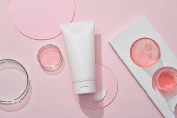 Background for the presentation of cosmetic products - white plastic tube container cream or cleanser with glassware filled pink liquid and some acrylic sheets on pink background