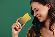 Enjoying Cashless Convenience. Woman Smiles As She Holds A Gold Credit Card In A Studio Setting